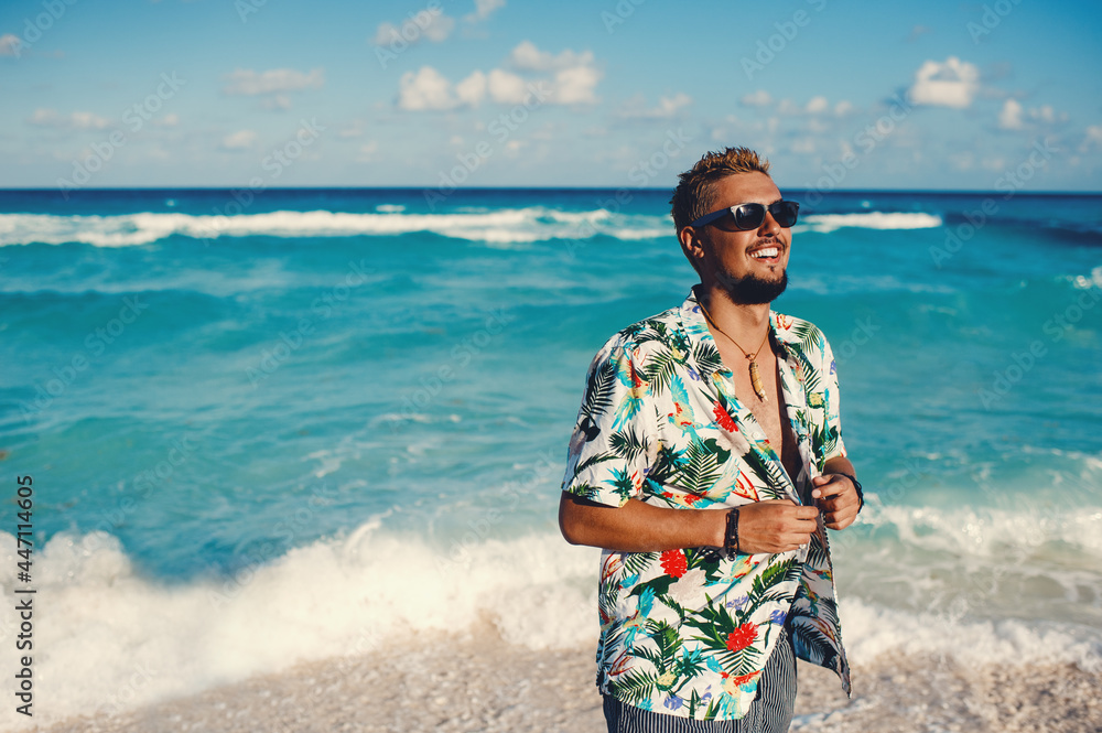 Handsome happy man wearing hawaiian shirt at the sea or the ocean background. Travel vacation holiday. Man walking at the sea, enjoy tropical season - obrazy, fototapety, plakaty 