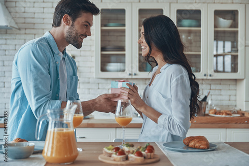 young man giving a gift box to his girlfriend while having breakfast at the domestic kitchen