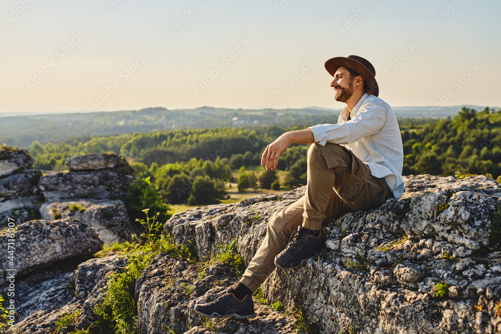 Happy young man sitting on rock enjoying the view on mountains