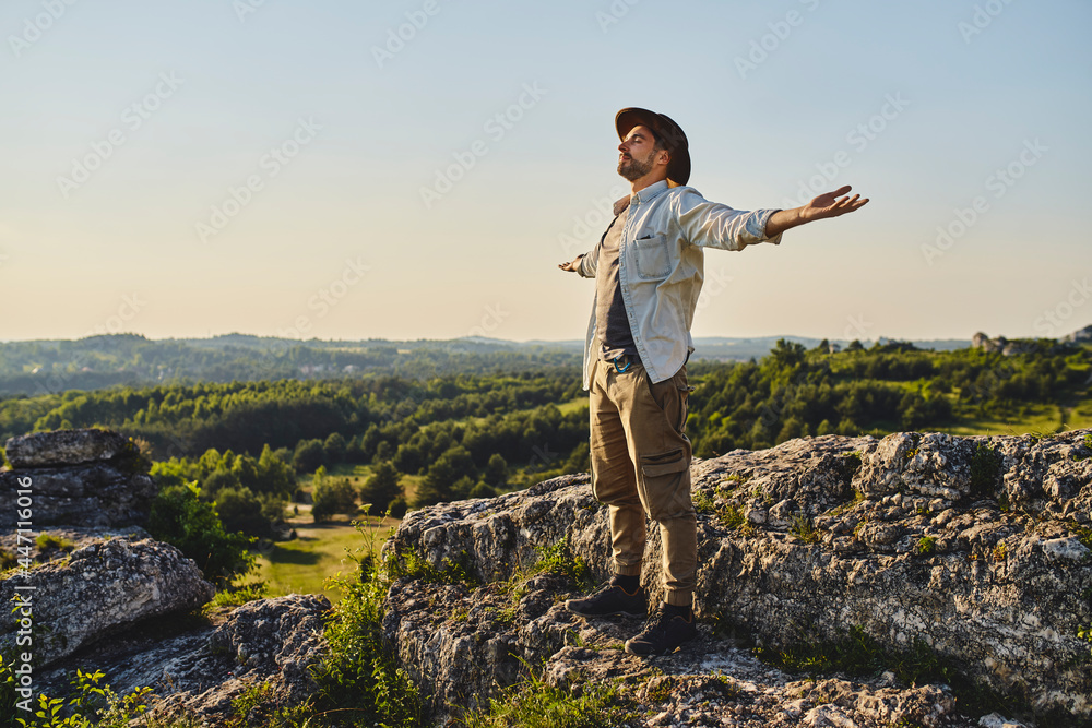 Naklejka premium Young man enjoying summer hiking standing with arms spread open