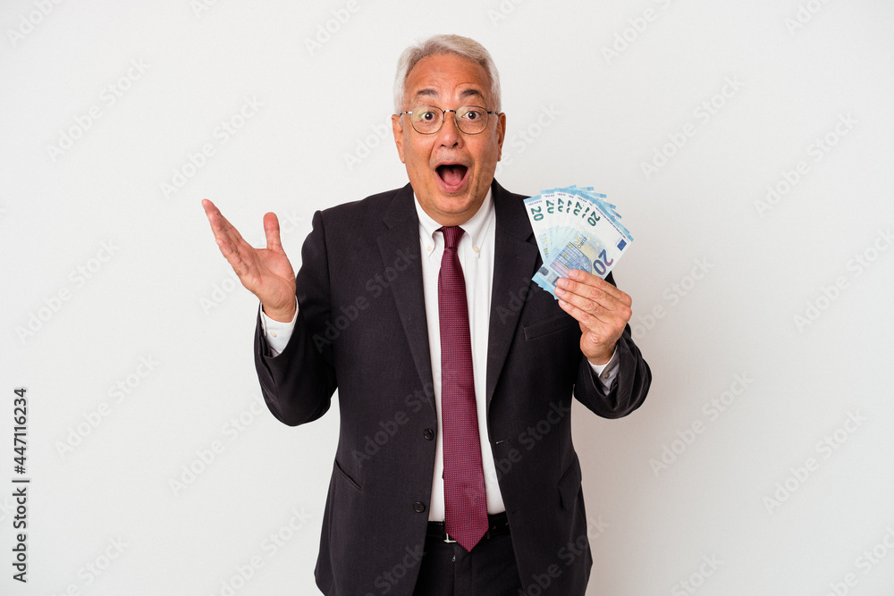 Senior american business man holding bills isolated on white background surprised and shocked. Senior american business man holding bills isolated on white background surprised and shocked.