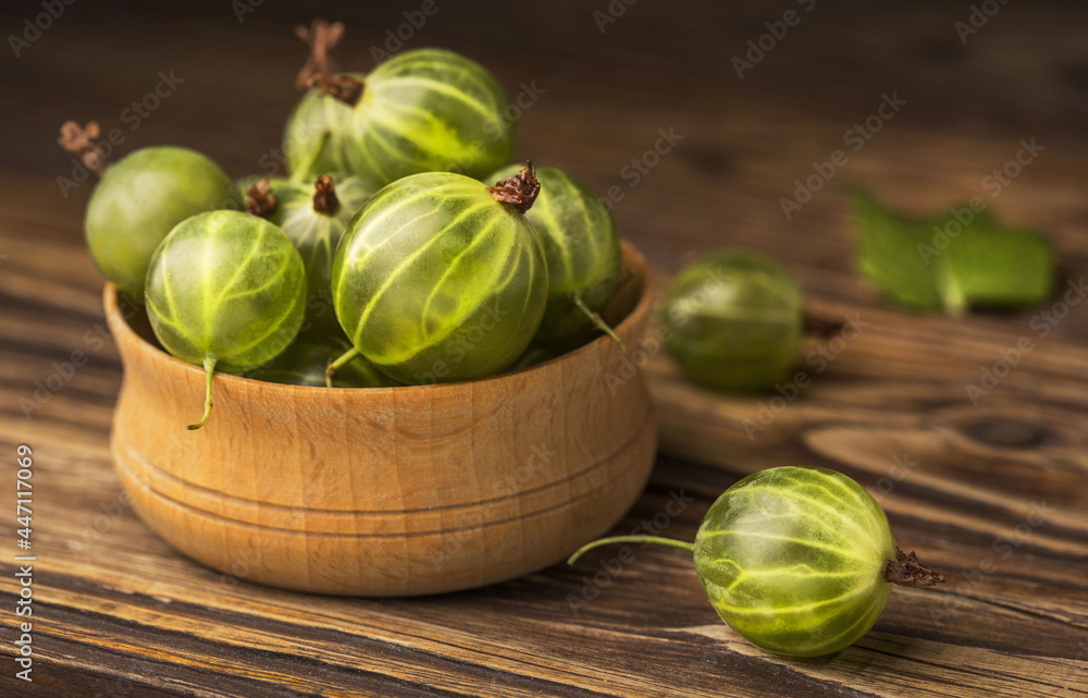 There is a beautiful wooden bowl with gooseberries on a wooden tabletop. There is a beautiful wooden bowl with gooseberries on a wooden tabletop.