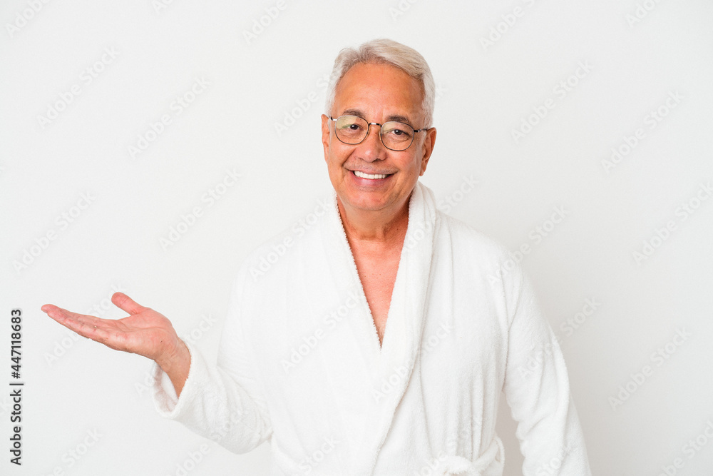 Senior american man wearing bathrobe isolated on white background showing a copy space on a palm and holding another hand on waist. Senior american man wearing bathrobe isolated on white background showing a copy space on a palm and holding another hand on waist.
