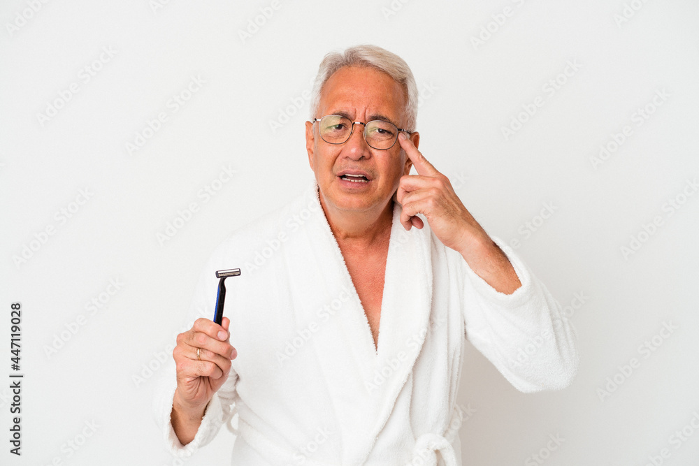 Senior american man wearing bathrobe holding razor blade isolated on white background showing a disappointment gesture with forefinger. Senior american man wearing bathrobe holding razor blade isolated on white background showing a disappointment gesture with forefinger.