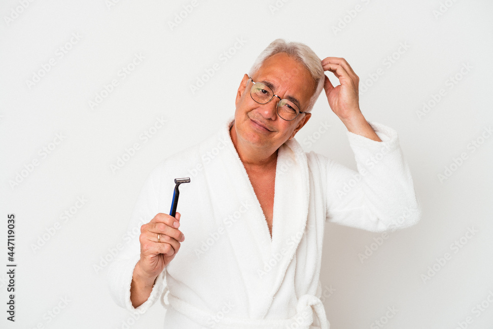 Senior american man wearing bathrobe holding razor blade isolated on white background being shocked, she has remembered important meeting.