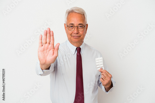 Senior american man holding pills isolated on white background standing with outstretched hand showing stop sign, preventing you. © Asier