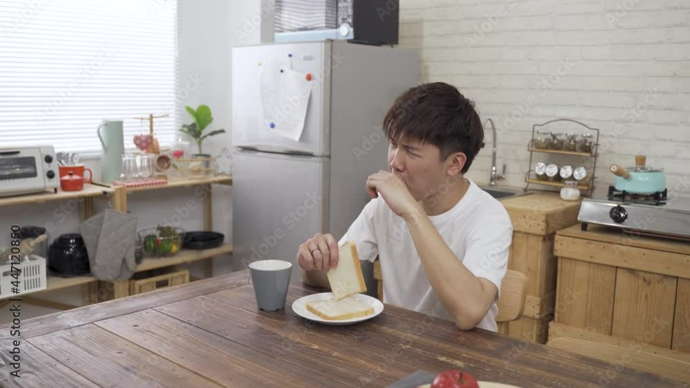 Asian japanese boy sitting at table alone is yawning while having toast and coffee for breakfast in the apartment. Asian japanese boy sitting at table alone is yawning while having toast and coffee for breakfast in the apartment.