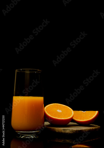 Orange juice in a glass with fruit slice hovering on the dark black background