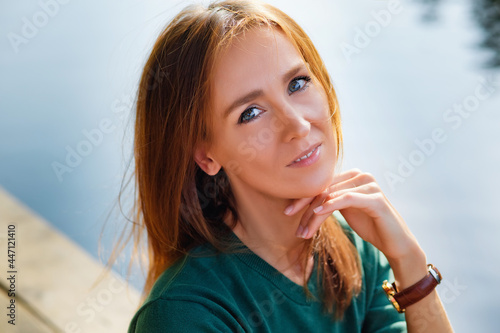 A young woman is sitting on an old bridge against the background of water. A positive portrait of a beautiful lady in a green sweater.