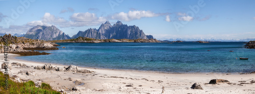 Beautiful picturesque Scandinavia panorama of a wide sandy beach on the shore of the blue calm bay of the Norwegian fjord with high rocky mountains on the horizon.