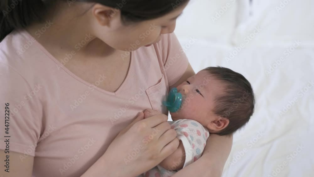 view from top japanese mom is looking and talking softly to her sleepy baby daughter in the arms while putting her to bed in the bedroom. view from top japanese mom is looking and talking softly to her sleepy baby daughter in the arms while putting her to bed in the bedroom.