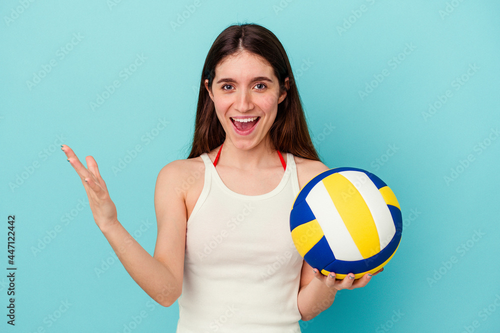 Young caucasian woman playing volleyball isolated on blue background receiving a pleasant surprise, excited and raising hands.