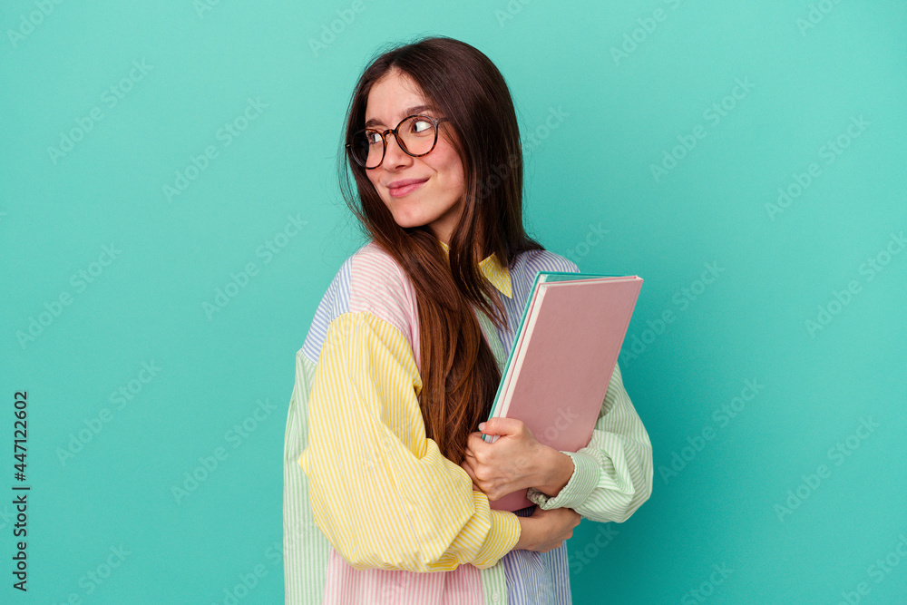 Young student caucasian woman isolated on blue background looks aside smiling, cheerful and pleasant. Young student caucasian woman isolated on blue background looks aside smiling, cheerful and pleasant.