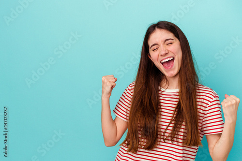 Young caucasian woman isolated on blue background raising fist after a victory, winner concept.