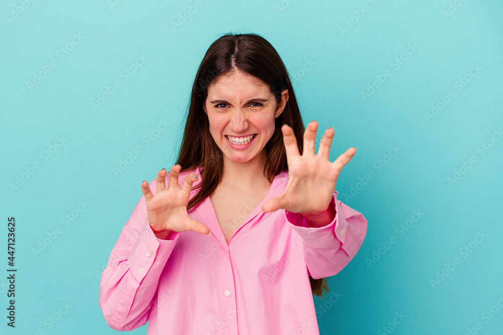 Young caucasian woman isolated on blue background showing claws imitating a cat, aggressive gesture. Young caucasian woman isolated on blue background showing claws imitating a cat, aggressive gesture.