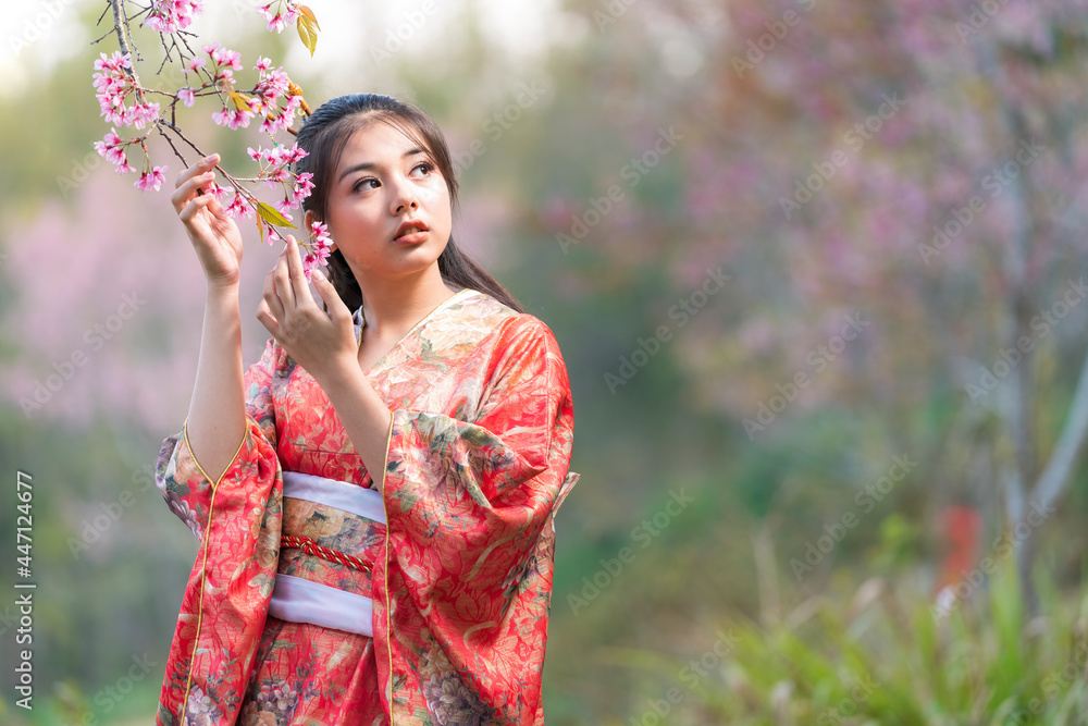 Japanese women wearing red kimonos. A young woman showing cherry blossoms on her hand under the tree in Japan. Japanese women wearing red kimonos. A young woman showing cherry blossoms on her hand under the tree in Japan.