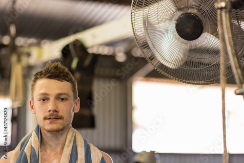 young male shearer with towel draped around neck enjoying cool air from fan