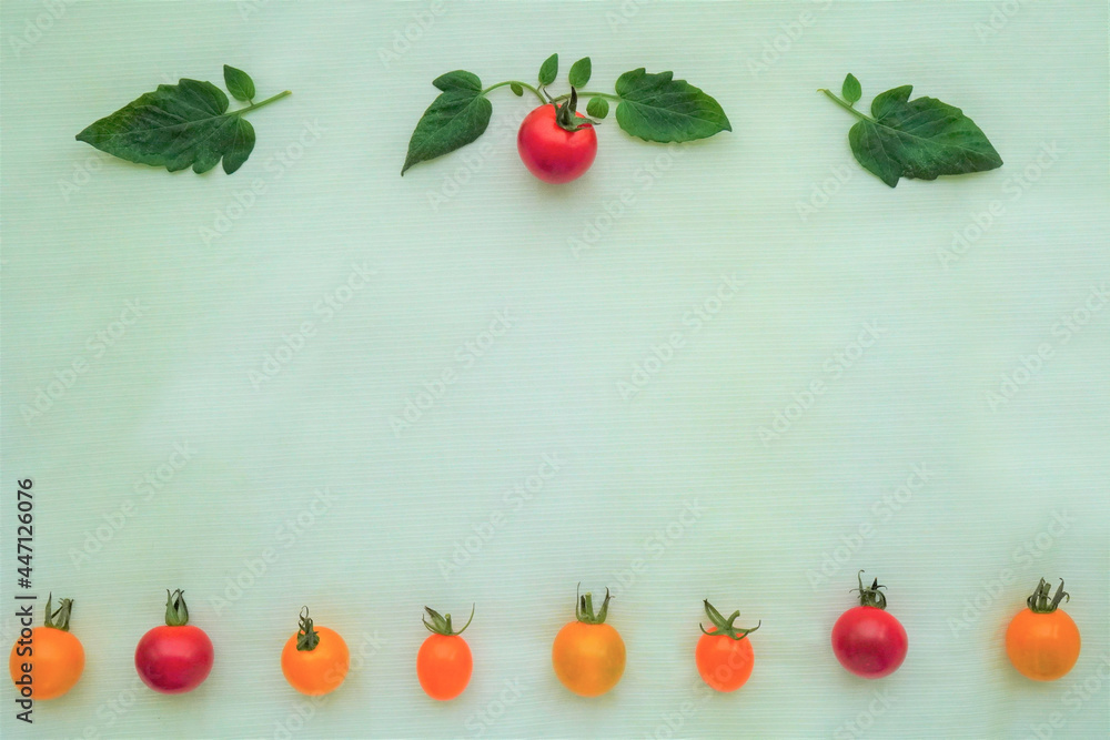 ペールグリーンのクロスを背景に上下に並んだ赤と黄のミニトマトと葉の飾り枠