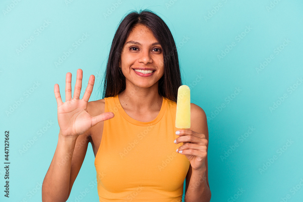 Young latin woman holding ice cream isolated on blue background smiling cheerful showing number five with fingers. Young latin woman holding ice cream isolated on blue background smiling cheerful showing number five with fingers.