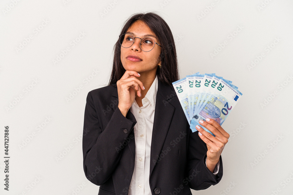 Young business latin woman holding bills isolated on white background looking sideways with doubtful and skeptical expression. Young business latin woman holding bills isolated on white background looking sideways with doubtful and skeptical expression.