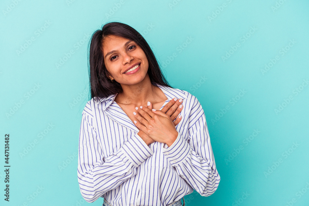 Fototapeta premium Young latin woman isolated on blue background has friendly expression, pressing palm to chest. Love concept.
