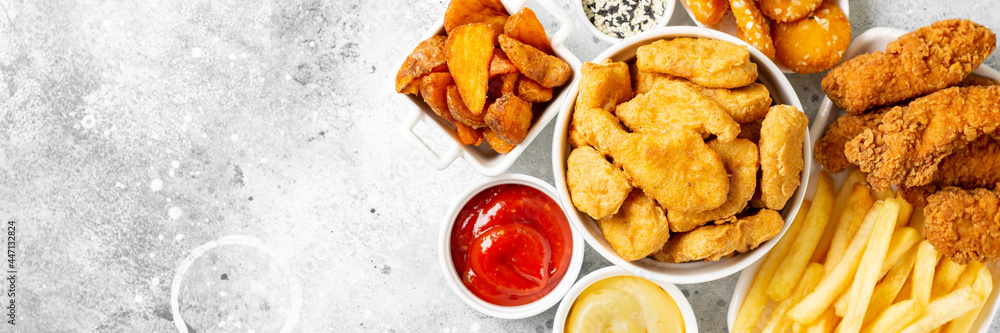 Chicken nuggets, strips, french fries, fried potatoes, ketchup and cheese sauce on a light background. Fast food top view with copyspace. Banner Chicken nuggets, strips, french fries, fried potatoes, ketchup and cheese sauce on a light background. Fast food top view with copyspace. Banner