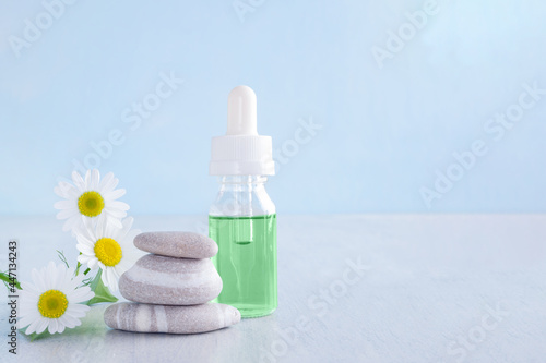 green liquid in a glass bottle with chamomile and stones