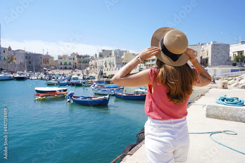 Holidays in Apulia. Back view of tourist girl wearing hat and looking at Giovinazzo picturesque harbor in Apulia, Italy.