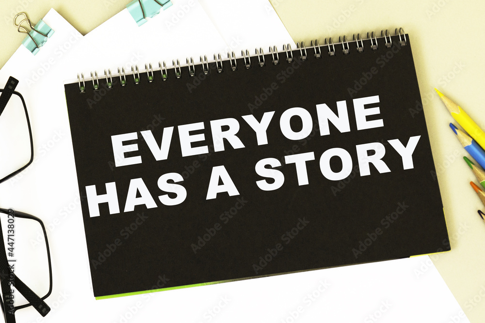 EVERYONE HAS A STORY. Office supplies, alarm clock, block with text. Business, education concept. flat lay EVERYONE HAS A STORY. Office supplies, alarm clock, block with text. Business, education concept. flat lay