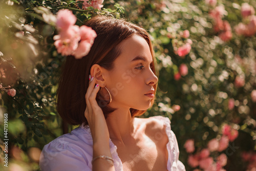 Foto Summer street style, fashion portrait of beautiful brunette woman with elegant bob hairstyle,  wearing white blouse, posing in street, near blooming roses
