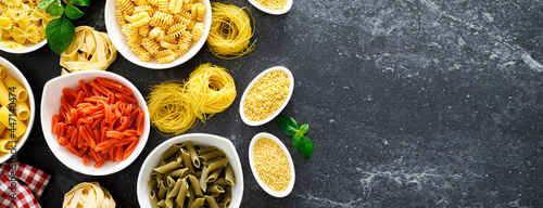 Pasta. Various kinds of uncooked pasta and noodles over stone background, top view with copy space for text. Italian food culinary concept. Collection of different raw pasta on cooking table. Banner.