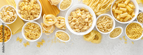 Pasta. Various kinds of uncooked pasta and noodles over stone background, top view with copy space for text. Italian food culinary concept. Collection of different raw pasta on cooking table. Banner.