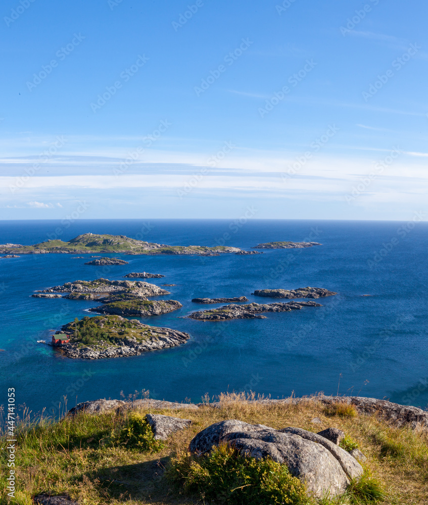 Aerial view of rocks in sea, blue sky in Lofoten Islands, Norway. Summer vertical landscape with small islands in blue water. View from top of cliff at shore.