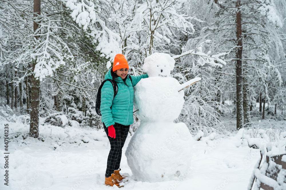 A portrait of happy beautiful woman wearing warm winter cloths enjoying the snowman preparation in a landscape