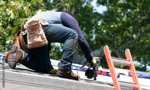 Contractor using nail gun replacing roof shingles on a roof