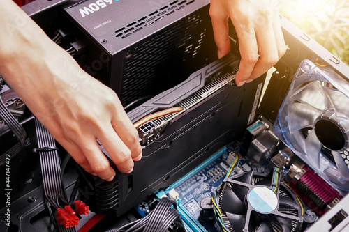 Plakat hand plugging a video card while maintenance personal computer hardware with selective focus.