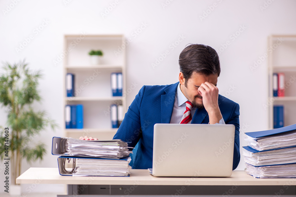 Young male employee unhappy with excessive work in the office Young male employee unhappy with excessive work in the office