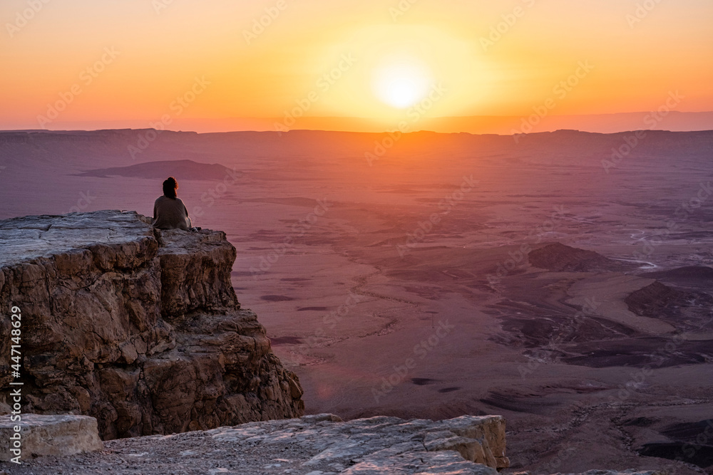 Woman sitting on the rim of the Ramon Crater in the negev desert at sunrise