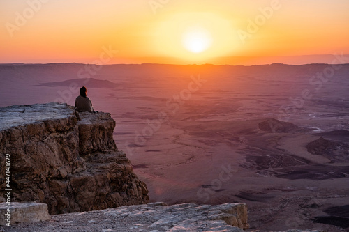 Woman sitting on the rim of the Ramon Crater in the negev desert at sunrise