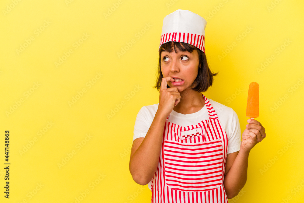 Young mixed race ice cream maker woman holding an ice cream isolated on yellow background relaxed thinking about something looking at a copy space. Young mixed race ice cream maker woman holding an ice cream isolated on yellow background relaxed thinking about something looking at a copy space.