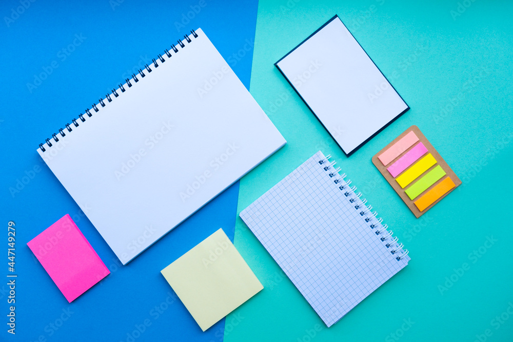 Flat lay with spiral notepad, notebook, sticker, and office supplies on blue background. Back to school concept. Top view. Flat lay with spiral notepad, notebook, sticker, and office supplies on blue background. Back to school concept. Top view.