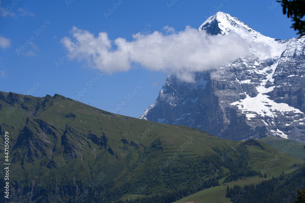 Mountain peak Eiger at Bernese highland on a sunny summer day with blue sky background and clouds in the foreground. Photo taken July 20th, 2021, Lauterbrunnen, Switzerland.