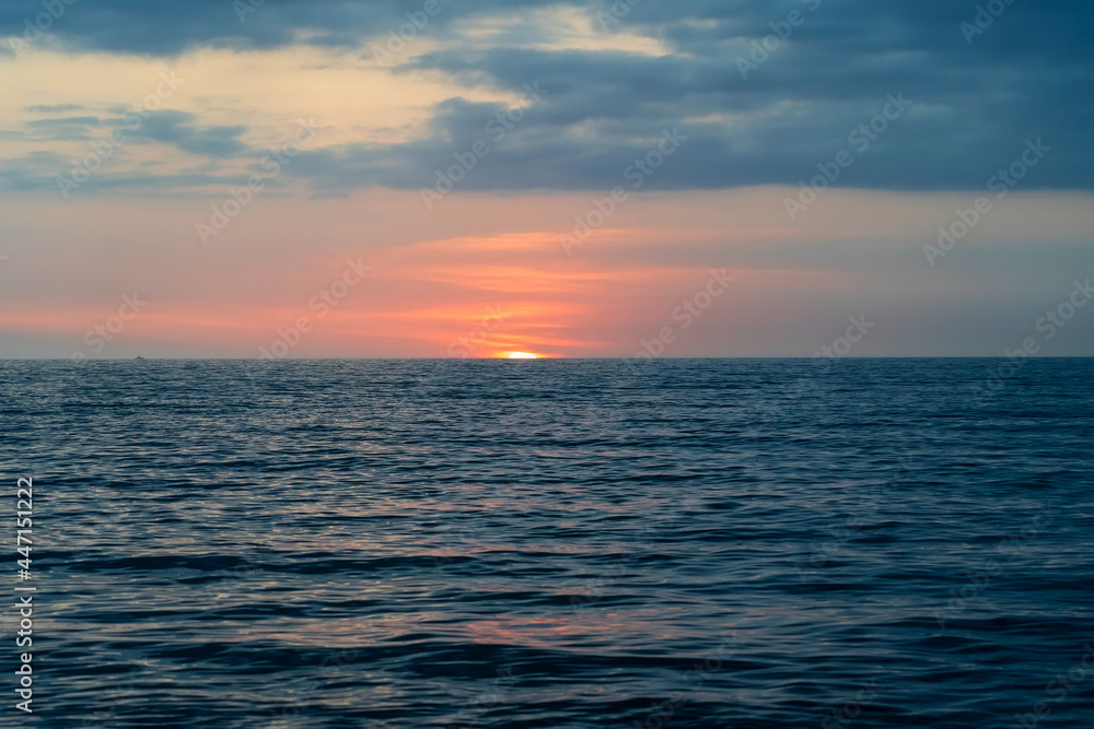 Calm sea with sunset sky and sun through clouds over. Meditation ocean and sky background. Tranquil seascape. Horizon over water.