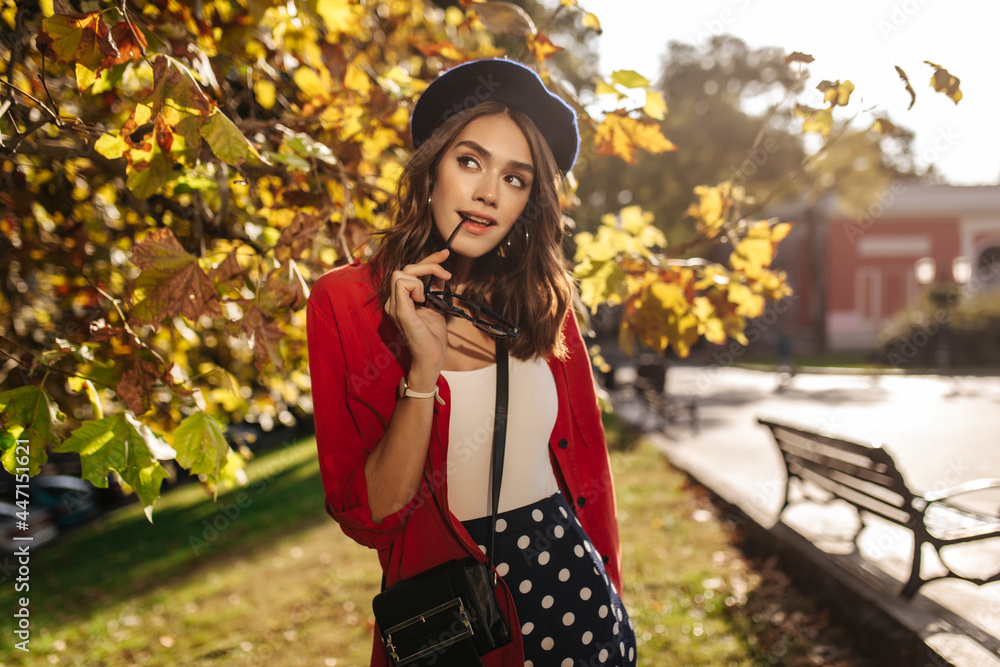 Attractive young woman with brunette hair, beret, white top and red shirt, posing outdoors, thoughtfully looking away. Sunny autumn city background Attractive young woman with brunette hair, beret, white top and red shirt, posing outdoors, thoughtfully looking away. Sunny autumn city background