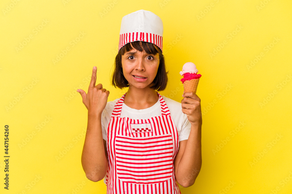 Young mixed race ice cream maker woman holding an ice cream isolated on yellow background showing a disappointment gesture with forefinger. Young mixed race ice cream maker woman holding an ice cream isolated on yellow background showing a disappointment gesture with forefinger.