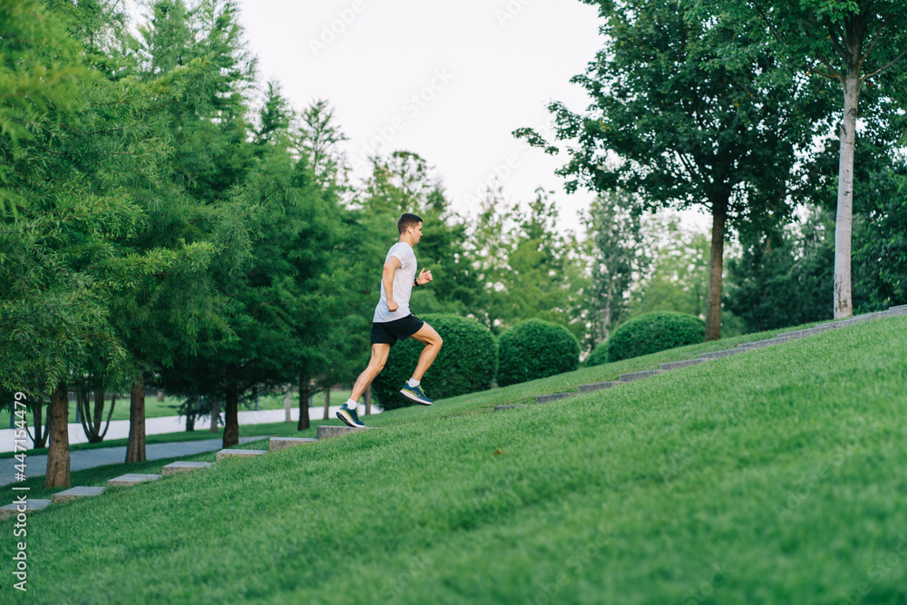 Attractive man athlete wearing sportswear run in park at summer up the stairs
