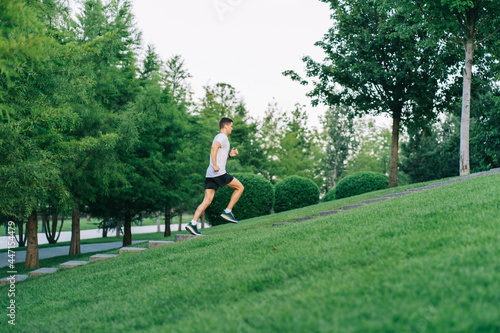 Attractive man athlete wearing sportswear run in park at summer up the stairs