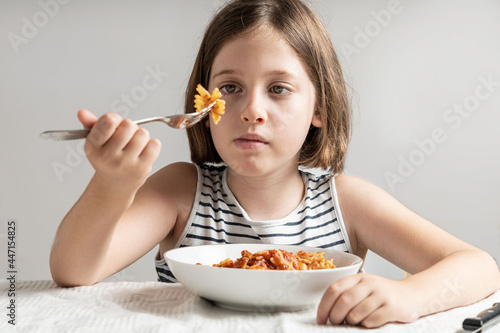 Cute litte girl eating pasta with tomato sauce with isalate gray background