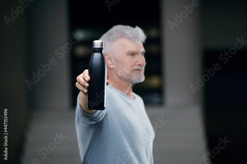 good looking gray haired senior man in white shirt with water bottle. Sport and health care concept.