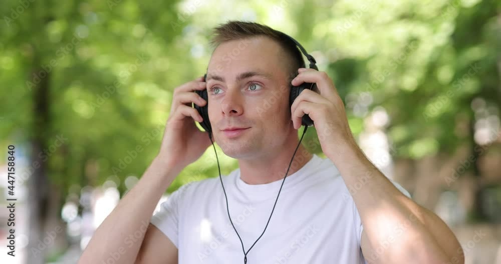 Smiling man puts on big headphones in the summer city, slow motion 4k at 120fps Smiling man puts on big headphones in the summer city, slow motion 4k at 120fps